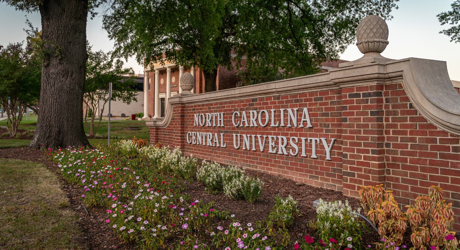 Red brick sign with North Carolina Central University letters next to a colorful flower garden