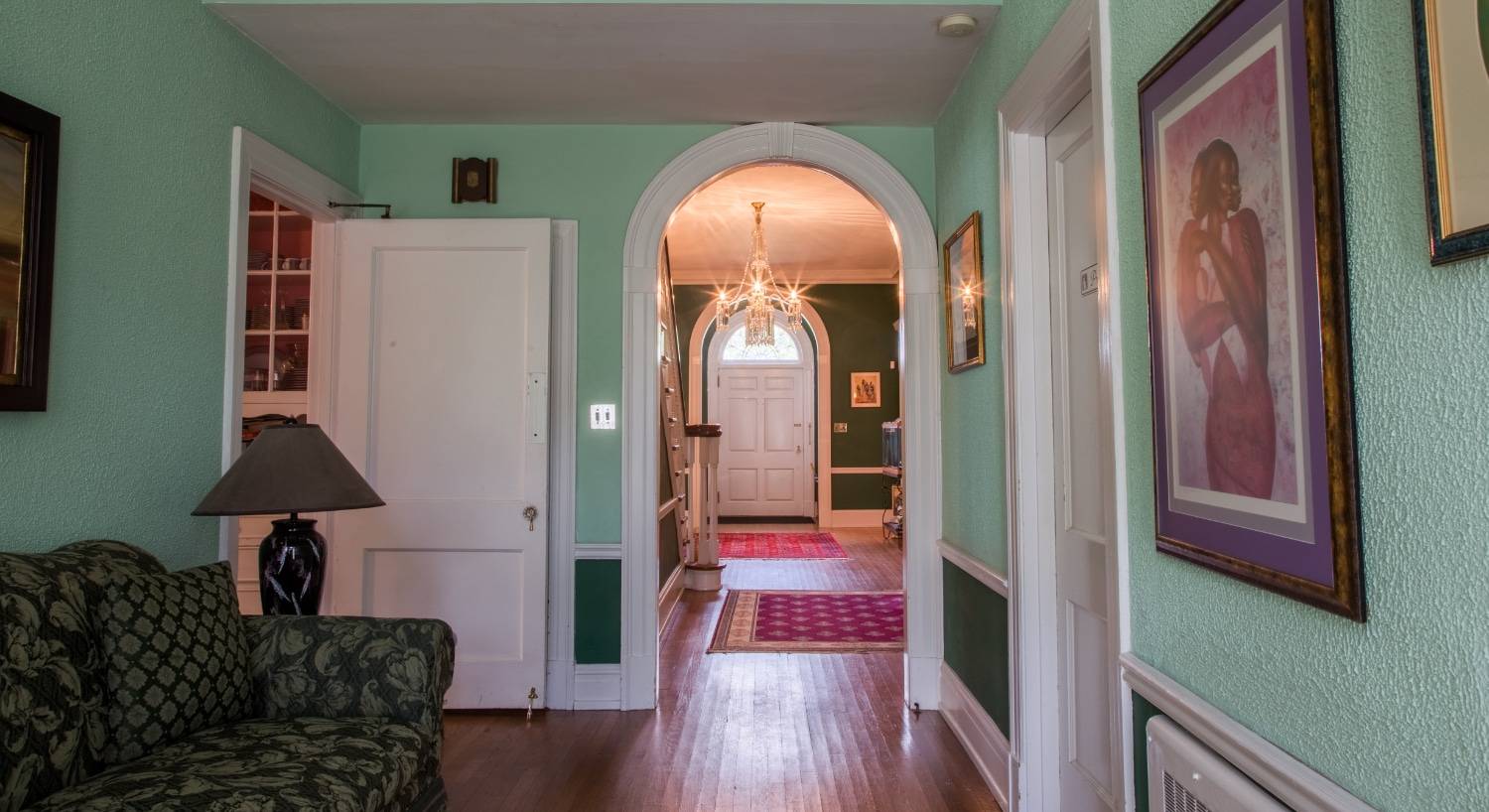 Jacob’s Library with light green walls, dark green wainscoting, hardwood floors, and a floral sofa