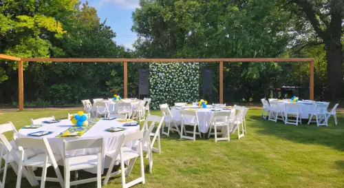 Backyard space set up for an event with multiple round tables with white tablecloths and white chairs