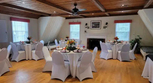 Large room with white panel walls, hardwood flooring, fireplace, and multiple round tables and chairs