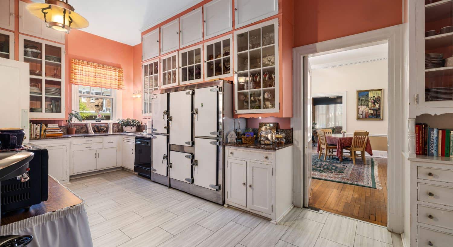 Kitchen with salmon walls, white cabinets, and dining room view