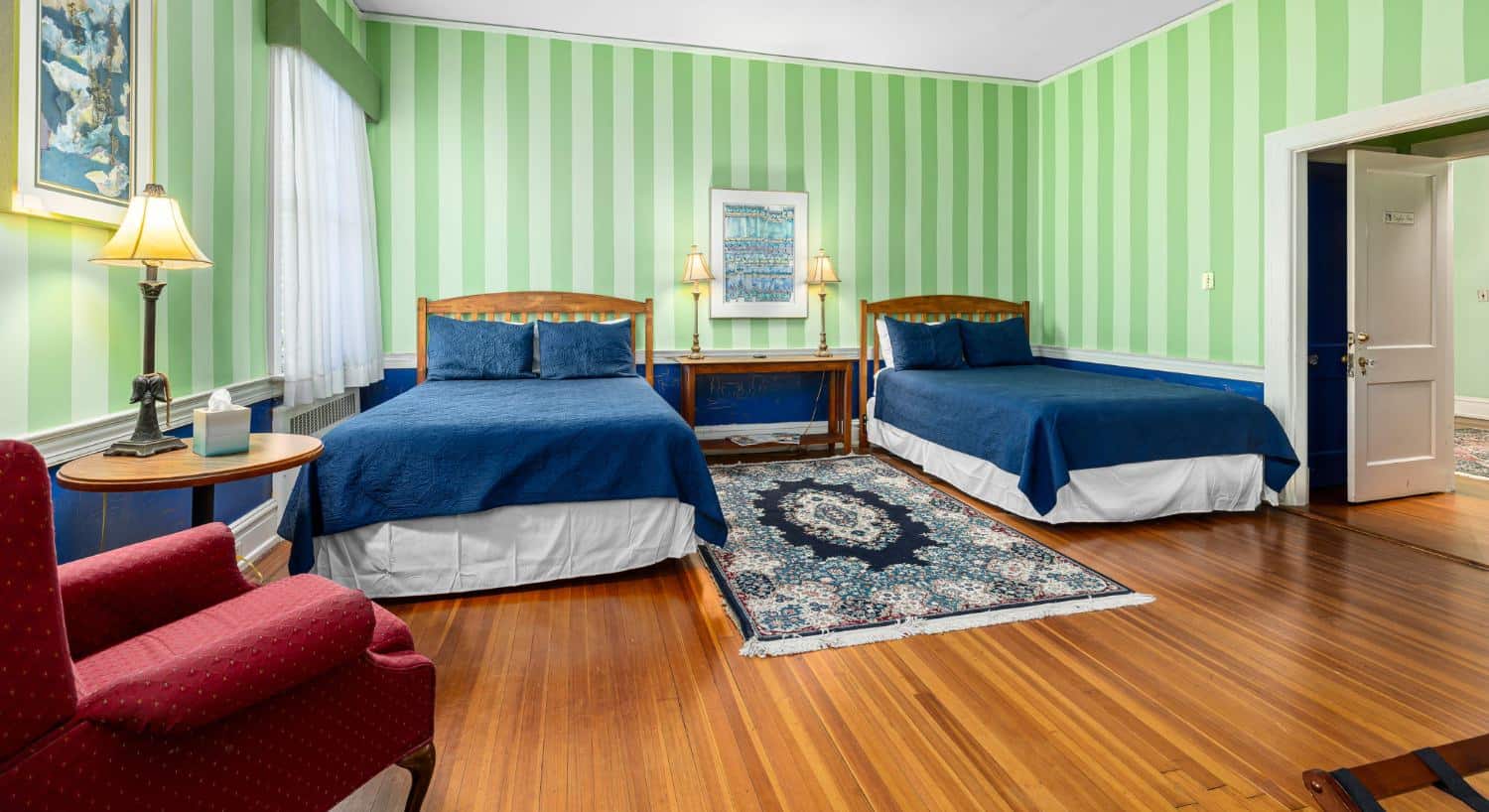 The Eagle’s Inn bedroom with striped green walls, two beds with navy bedding, and red armchair
