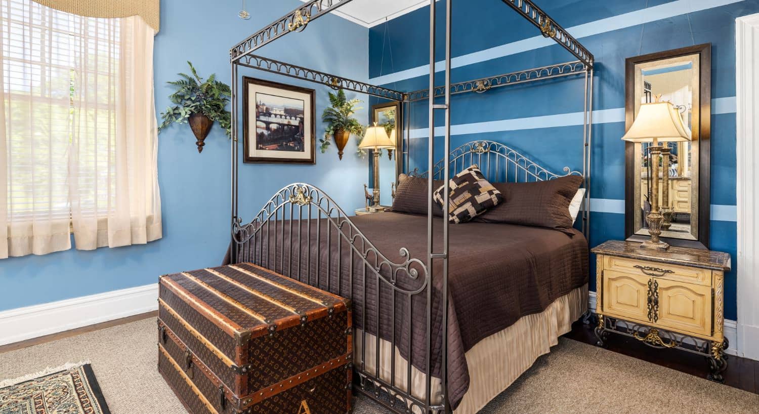 The Tiger Room bedroom with blue walls, hardwood flooring, wrought iron canopy bed, and chaise lounge