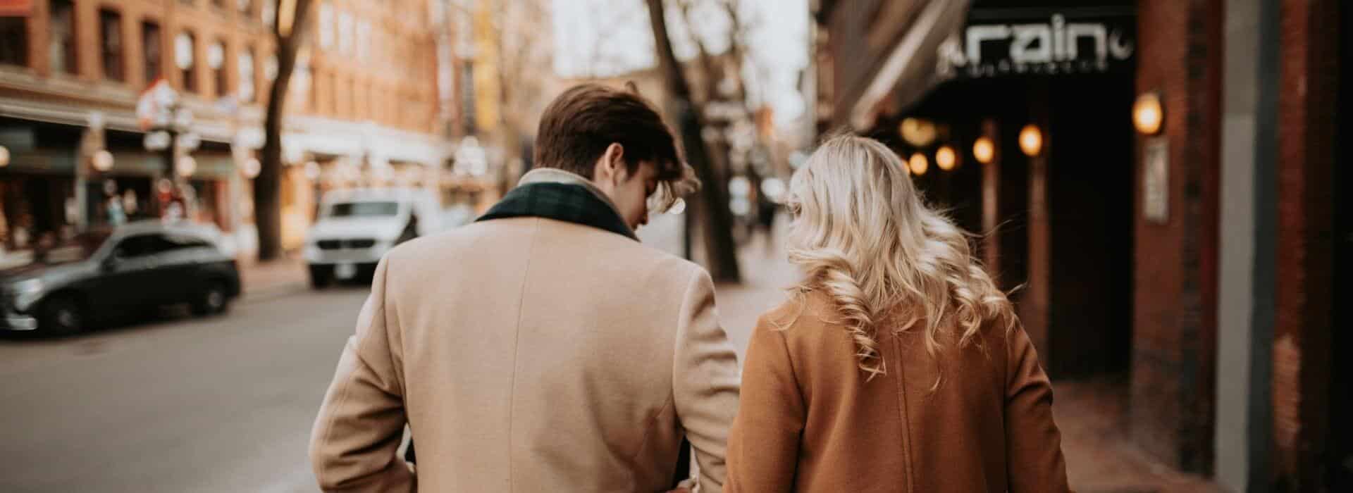 Couple walking arm in arm down a city street in winter.