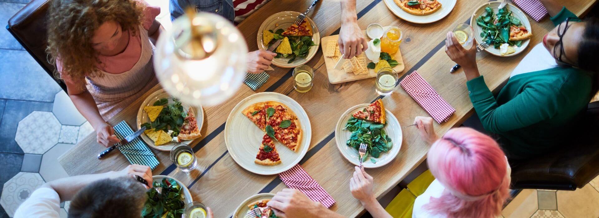 Group of people sharing pizza and salad at a dining table.