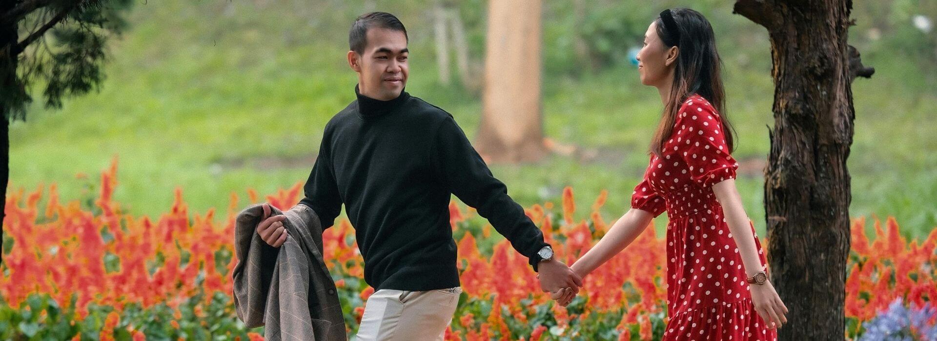 A couple walks hand in hand through a garden filled with vibrant flowers during a peaceful outdoor stroll.